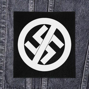 Peut inclure: Un écusson carré noir avec un symbole blanc de croix gammée barrée par une ligne diagonale, sur un fond de veste en jean. Le patch est une déclaration visuelle forte.