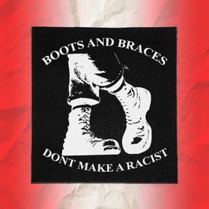 May include: A square black fabric patch featuring a white graphic illustration of legs wearing cuffed jeans and boots. The text "BOOTS AND BRACES" is arched above the illustration, and the text "DONT MAKE A RACIST" is arched below it.