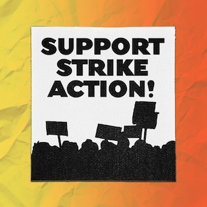 May include: A square white fabric patch featuring the black text SUPPORT STRIKE ACTION! above a black silhouette graphic of a crowd of people holding protest signs. The design is printed on a textured white material with a visible woven fabric pattern.