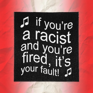 May include: A square black fabric patch featuring white text that reads, "if you're a racist and you're fired, it's your fault!" with a musical note symbol at the top left and bottom right corners, set against a textured red background.