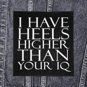 Puede incluir: Un parche cuadrado negro con texto blanco que dice "I HAVE HEELS HIGHER THAN YOUR IQ". El parche está sobre un fondo de chaqueta vaquera.