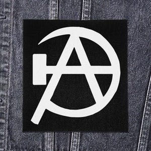 Op de afbeelding: Een zwarte vierkante patch met een wit anarchiesymbool, een gestileerde letter "A" in een cirkel, met een hamer en sikkel ontwerp. De patch is geplaatst tegen een denim jas achtergrond.