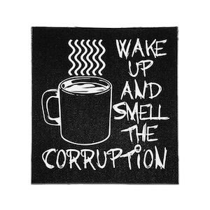 May include: A square black fabric patch featuring a white graphic of a coffee mug with steam rising from it. To the right and below the mug, the text reads WAKE UP AND SMELL THE CORRUPTION in a distressed, hand-drawn white font style.