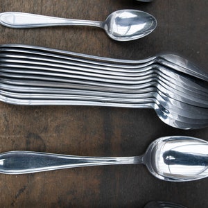May include: A stack of silver spoons, with one spoon on top and another spoon on the bottom. The spoons are arranged in a row, with the handles pointing to the right.