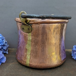 May include: Antique copper pot with a hammered finish and a brass handle. The pot has a worn, rustic look and is perfect for adding a touch of vintage charm to your kitchen.
