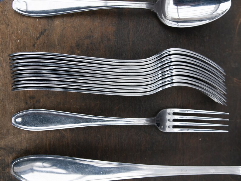 May include: A set of silverware, including a spoon, fork, and a stack of forks. The silverware is made of polished stainless steel and is arranged on a wooden surface.