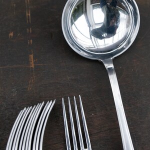 May include: A silver ladle with a shiny, reflective surface, a silver fork, and a set of silver forks on a dark wooden surface.