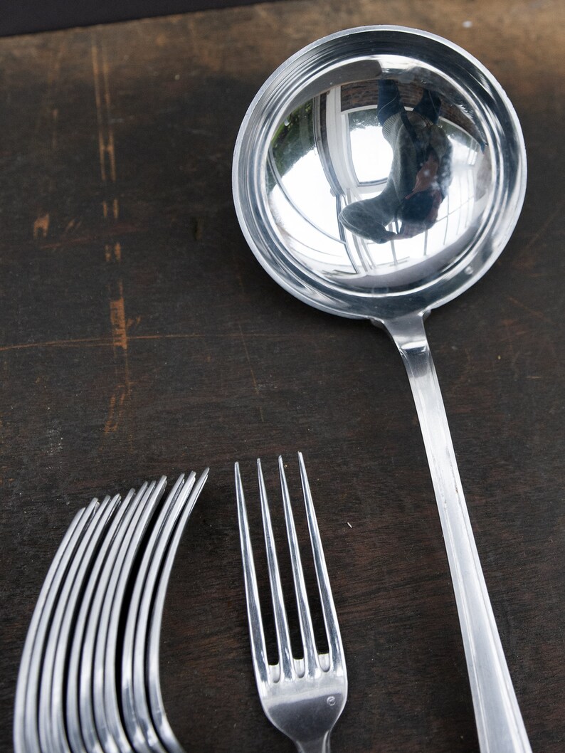 May include: A silver ladle with a shiny, reflective surface, a silver fork, and a set of silver forks on a dark wooden surface.