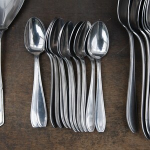 May include: A set of silver spoons, including a larger serving spoon, arranged on a wooden surface. The spoons are polished and reflect light.