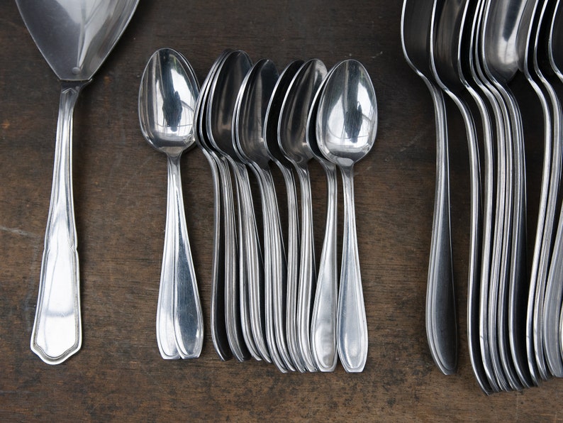May include: A set of silver spoons, including a larger serving spoon, arranged on a wooden surface. The spoons are polished and reflect light.