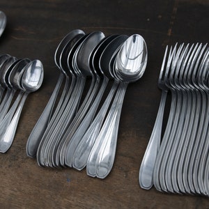 May include: A set of silver spoons and forks arranged in rows on a wooden surface. The spoons are all the same size and shape, while the forks are slightly different. The spoons and forks are all shiny and new.