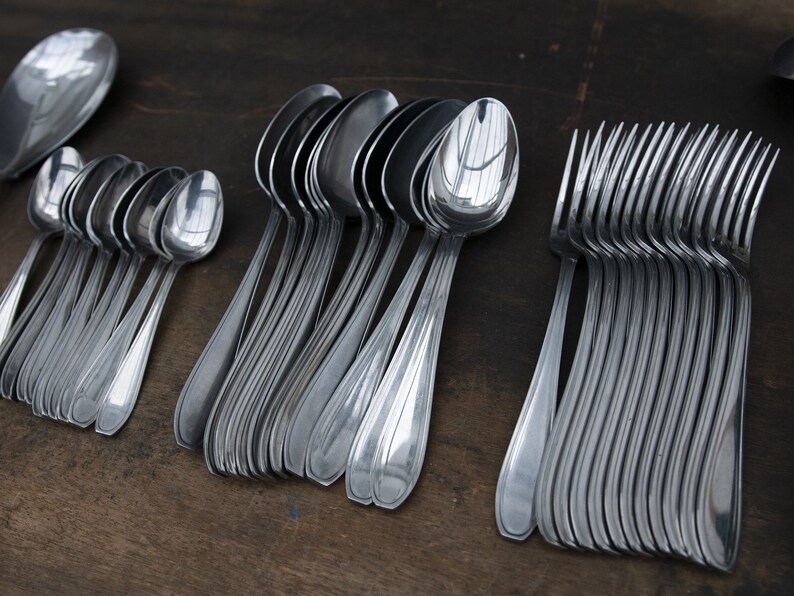May include: A set of silver spoons and forks arranged in rows on a wooden surface. The spoons are all the same size and shape, while the forks are slightly different. The spoons and forks are all shiny and new.