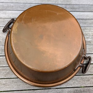 Op de afbeelding: Een grote bakvorm van koper met twee zwarte metalen handvatten. De vorm heeft een gehamerde afwerking en is licht aangetast.