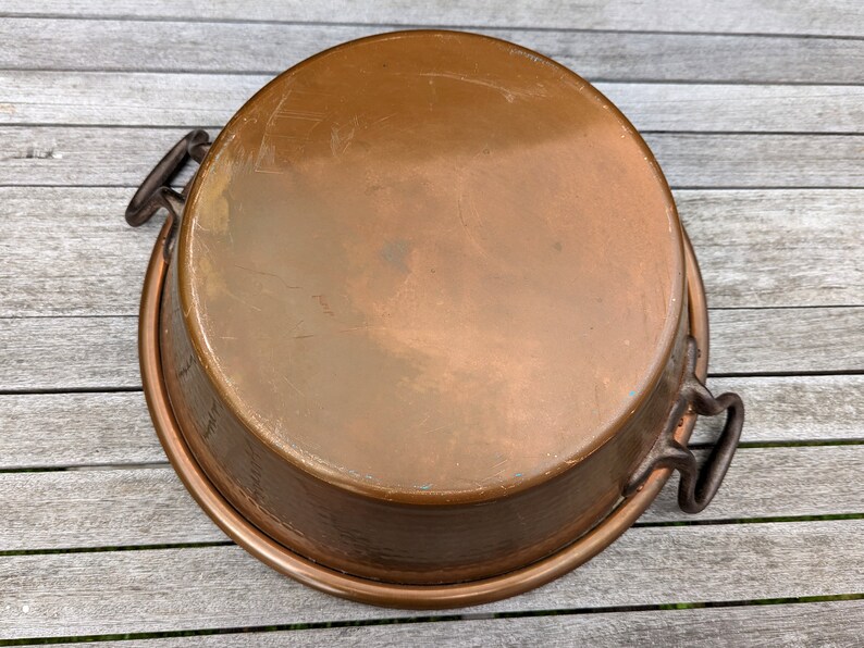 Op de afbeelding: Een grote bakvorm van koper met twee zwarte metalen handvatten. De vorm heeft een gehamerde afwerking en is licht aangetast.