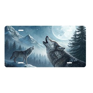 May include: License plate featuring a detailed illustration of two wolves howling at the moon in a snowy mountain landscape. The plate has a rectangular shape with pre-drilled holes for mounting.