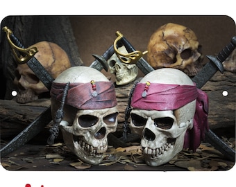 Peut inclure: Deux figurines de crânes de pirates avec des bandanas rouges, des épées croisées et un fond en bois.