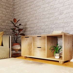 May include: A light wood cabinet with two drawers and a shelf. The cabinet has a natural wood finish and is sitting on a light wood floor. There is a plant in a white pot on the shelf.