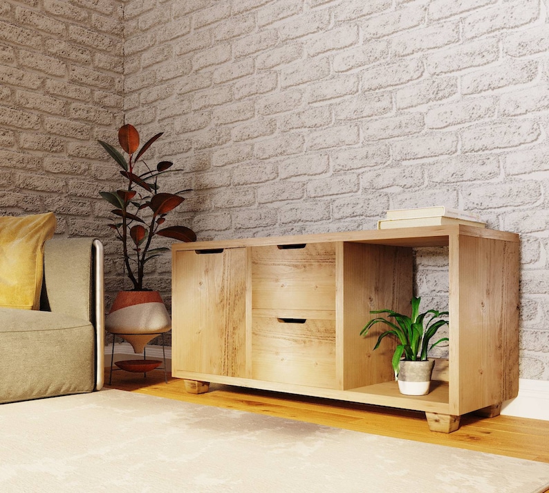 May include: A light wood cabinet with two drawers and a shelf. The cabinet has a natural wood finish and is sitting on a light wood floor. There is a plant in a white pot on the shelf.