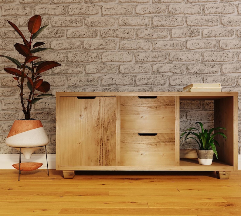 May include: A wooden cabinet with two drawers and a door. The cabinet has a light wood finish and is sitting on a wooden floor. There is a plant in a pot on the top shelf of the cabinet.