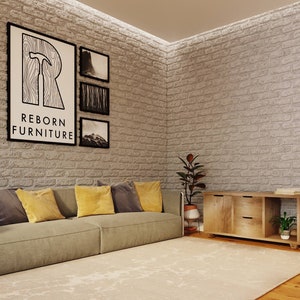 May include: A light brown wooden cabinet with two drawers and a shelf. The cabinet has a rustic look and is sitting on a light brown wooden floor. The cabinet is in front of a white brick wall with a gray couch and yellow pillows. There are three black framed pictures on the wall with the text "REBORN FURNITURE" on the largest picture.