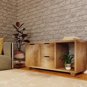 May include: A wooden cabinet with two drawers and an open shelf. The cabinet is light brown and has a rustic finish. There are two potted plants on either side of the cabinet.
