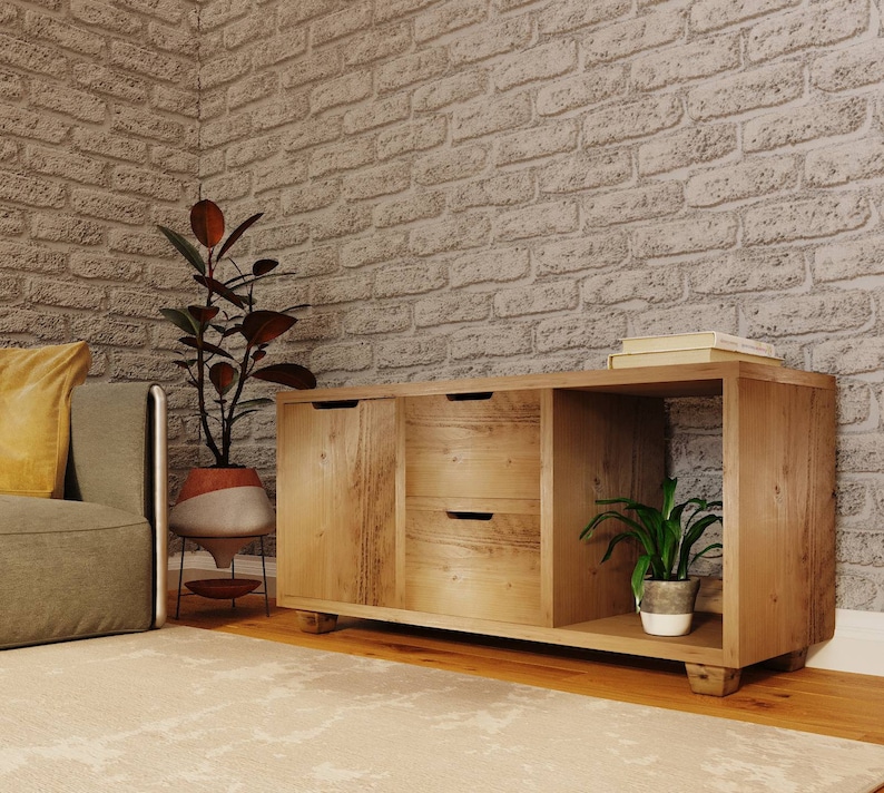 May include: A wooden cabinet with two drawers and an open shelf. The cabinet is light brown and has a rustic finish. There are two potted plants on either side of the cabinet.