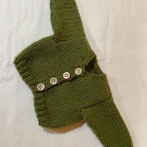 May include: A green knitted cardigan with button closures. The cardigan is made of a soft, textured yarn and has a relaxed fit.