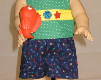 Puede incluir: Una muñeca con un vestido verde y amarillo con lunares blancos y una falda con estampado de estrellas azules y blancas. La muñeca sostiene un juguete de pez rojo.