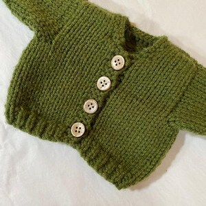 May include: A green knitted cardigan with five white buttons.
