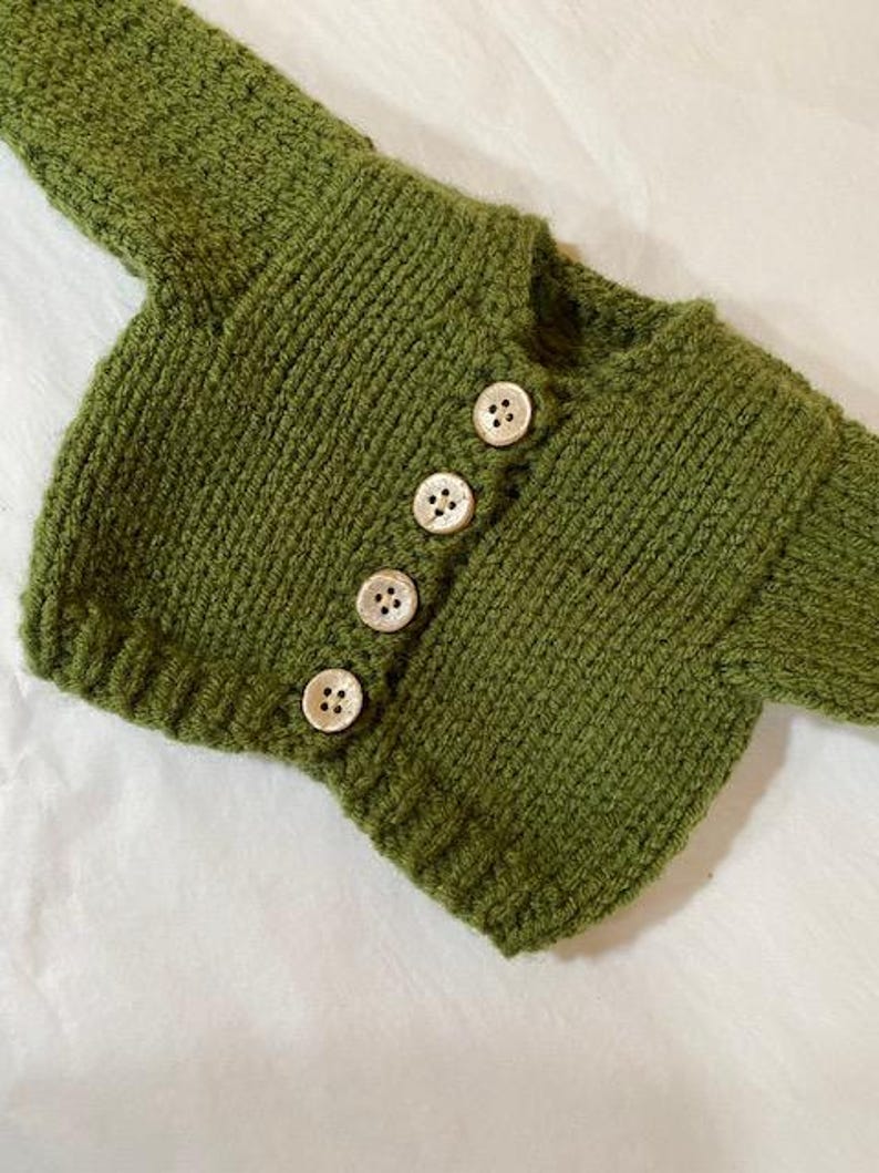 May include: A green knitted cardigan with five white buttons.