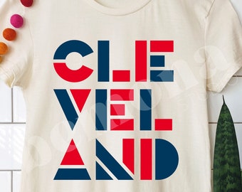Puede incluir: Una camiseta blanca con un diseño gráfico que dice "CLEVELAND" en letras rojas y azules.
