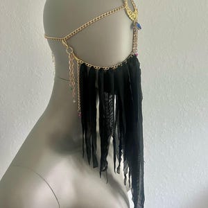 Könnte beinhalten: Ein goldfarbenes Kopfstück mit Kettenmuster, das einen Halbmond und herabhängende Ketten aufweist. Schwarzer Stoff drapiert von der Kette, verziert mit kleinen, farbigen Perlen. Das Kopfstück wird auf einer Schaufensterpuppe präsentiert.