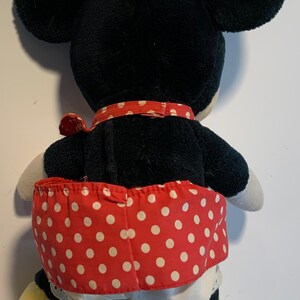 May include: A black and red plush toy with a white polka dot skirt. The toy has large ears and yellow shoes.