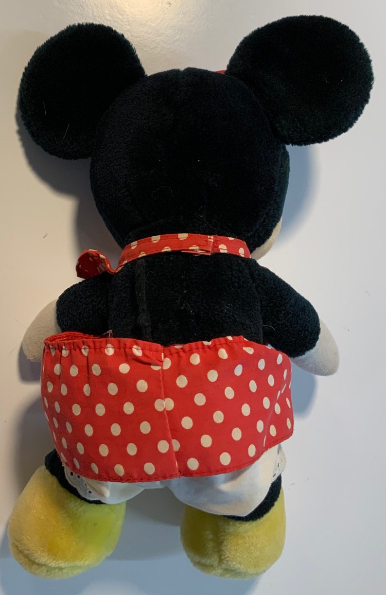 May include: A black and red plush toy with a white polka dot skirt. The toy has large ears and yellow shoes.