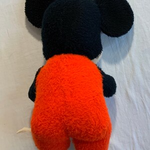 Puede incluir: Un juguete de peluche de Mickey Mouse con un mono rojo. El juguete est&aacute; de espaldas a la c&aacute;mara, con la espalda y una de sus orejas visibles.