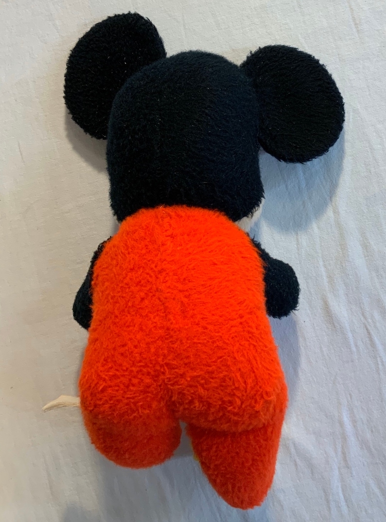Puede incluir: Un juguete de peluche de Mickey Mouse con un mono rojo. El juguete est&aacute; de espaldas a la c&aacute;mara, con la espalda y una de sus orejas visibles.