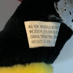 May include: A black and yellow stuffed animal with a white lace trim. The tag reads "ALL NEW MATERIALS-POLYESTER ME 1525:PA 1378:OHIO PA 137 CANASA TRADING CORP. BUB PRODUCT OF KOREA"