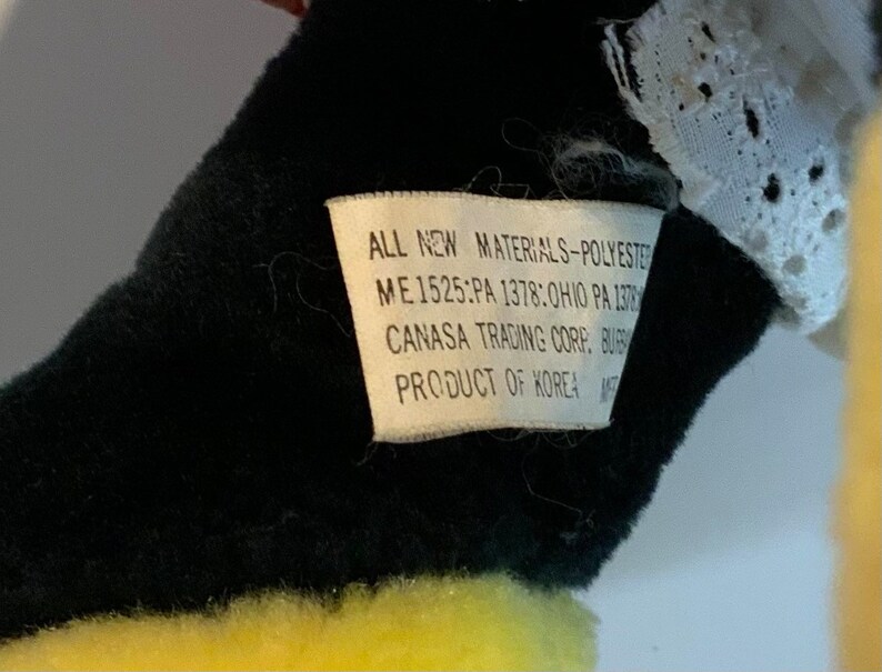 May include: A black and yellow stuffed animal with a white lace trim. The tag reads "ALL NEW MATERIALS-POLYESTER ME 1525:PA 1378:OHIO PA 137 CANASA TRADING CORP. BUB PRODUCT OF KOREA"