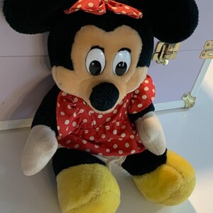 May include: A plush toy of Mickey Mouse's girlfriend Minnie Mouse. She is wearing a red dress with white polka dots and a red bow with white polka dots. She has large black eyes and a black nose.