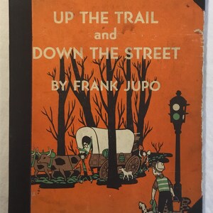 May include: An orange book cover with the title "Up the Trail and Down the Street" by Frank Jupo. The cover features an illustration of a covered wagon pulled by oxen, children walking, and a traffic light.