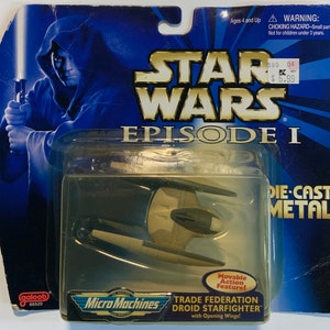 May include: A blue and tan die-cast metal Star Wars Episode I Trade Federation Droid Starfighter toy with opening wings. The toy is part of the Micro Machines series and is packaged in a blue and white box with a picture of a Jedi.