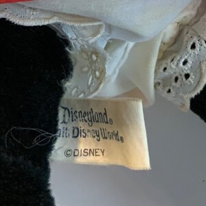 May include: Close-up of a white tag with black text that reads "Disneyland&reg; Walt Disney World&reg; &copy;DISNEY".