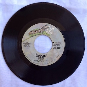 May include: A black vinyl record with a label featuring a caterpillar on a leaf, the text "bread DIARY (D. Gates)", and the song title "EK-45784-A".