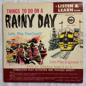 Puede incluir: Una portada de disco de vinilo vintage con una ilustración colorida de bomberos apagando un incendio y un tren en una vía. La portada se titula "Things to do on a Rainy Day" y presenta el texto "Let's Play Fire Chief!" y "Let's Play Engineer!" El disco es un disco "Listen & Learn" y equivale a tres discos de 45 RPM. La portada también incluye el texto "Fun for Children from 2 to 6" y "Stimulates Play Activities and Teaches Safety".