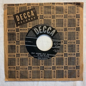May include: A black and white 7-inch vinyl record with the title "Ole Moses Put Pharaoh In His Place" by Fred Waring. The record is on a brown paper sleeve with the Decca Records logo and the words "Unbreakable 45 RPM Record" printed on it.