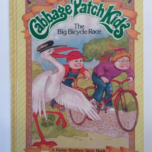 Könnte beinhalten: Ein gelber Buchumschlag mit dem Titel "Cabbage Patch Kids The Big Bicycle Race" und einem Bild von drei Cabbage Patch Kids, die Fahrrad fahren. Das Buch ist ein Parker Brothers Story Book mit dem Autor und Illustrator, die auf dem Cover aufgeführt sind.