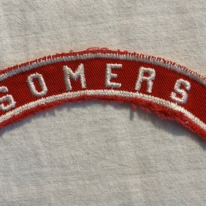 Op de afbeelding: Rode en witte geborduurde patch met het woord "SOMERS" in witte letters.