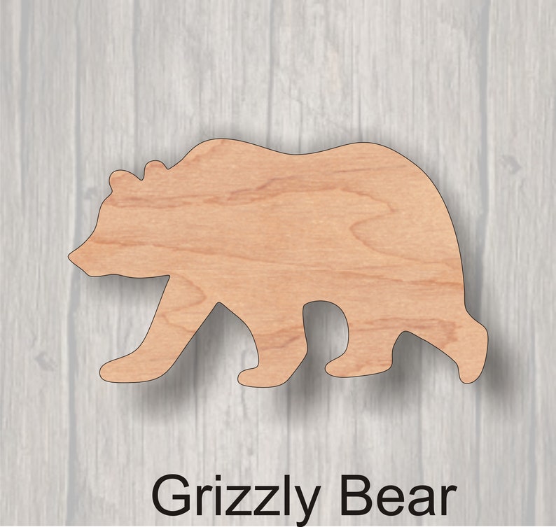 May include: Wooden cutout of a grizzly bear in a walking pose. The bear is made of light brown wood and is a simple silhouette.