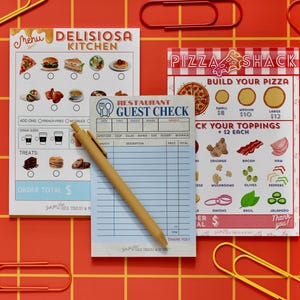 May include: A collection of restaurant-themed stationery on a red grid background. Includes a menu, a guest check notepad, and a pizza-themed menu. A yellow pen and colorful paper clips are also present.