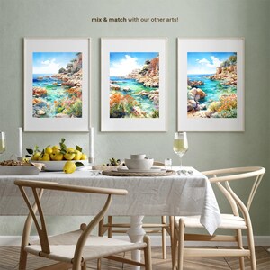 May include: Three framed watercolor paintings of a coastal scene with turquoise water, rocky cliffs, and lush greenery. The paintings are displayed on a light green wall above a dining table with a white tablecloth, wooden chairs, and a bowl of lemons.